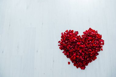 Beyaz ahşap arka planda kırmızı gül yapraklarının kalbi.