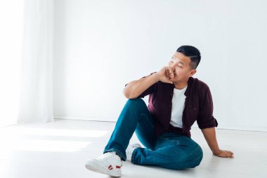 Güzel Asyalı bir adam beyaz bir odada yerde oturuyor.