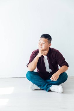Güzel Asyalı bir adam beyaz bir odada yerde oturuyor.