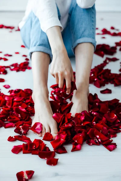 Womens feet and the red rose petals — Stock Photo, Image