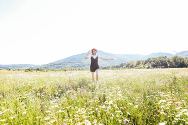 Güzel, genç, mutlu bir kadın papatya tarlasında koşuyor.