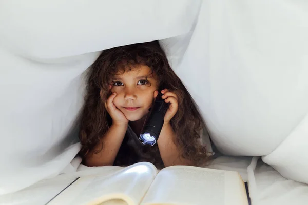 Klein meisje leest een boek met een zaklamp in bed — Stockfoto