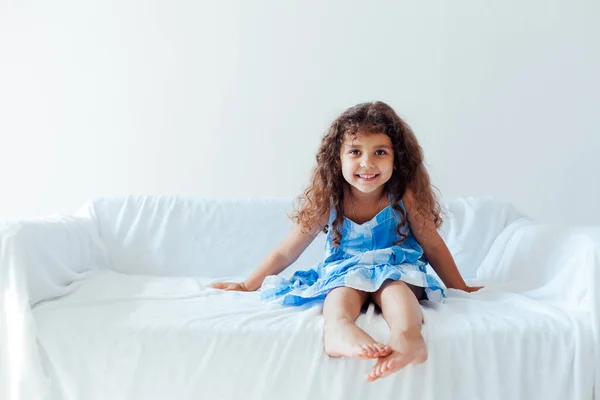 Bambina vestita di blu su un divano bianco — Foto Stock