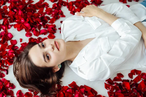 Piękna kobieta leży wśród czerwonych płatków kwiatów róż — Zdjęcie stockowe