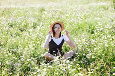 Güzel bir kadın papatya tarlasında çimlerde oturur.