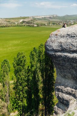 Esmer kadın uçurumun kenarında oturmuş yolculuğun doğasına bakıyor.