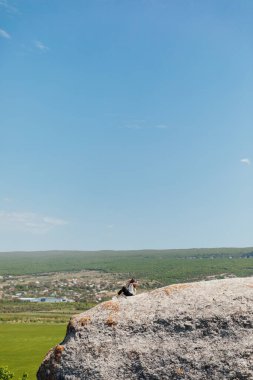 Esmer kadın uçurumun kenarında oturmuş yolculuğun doğasına bakıyor.