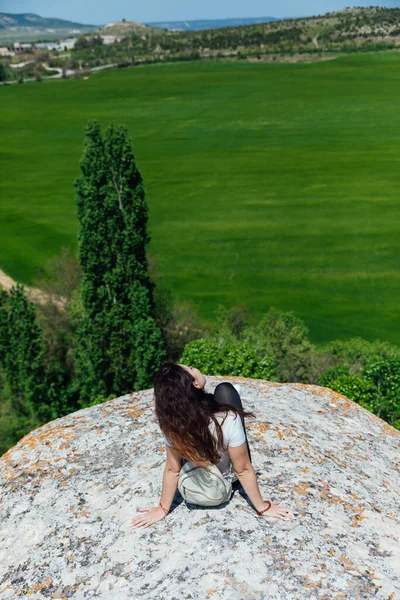 Esmer kadın uçurumun kenarında oturmuş yolculuğun doğasına bakıyor.