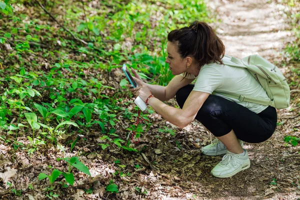 Uma mulher bonita tira fotos em um smartphone em uma floresta verde — Fotografia de Stock
