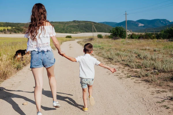 Mère et fils marchent le long de la route rurale vers le champ — Photo