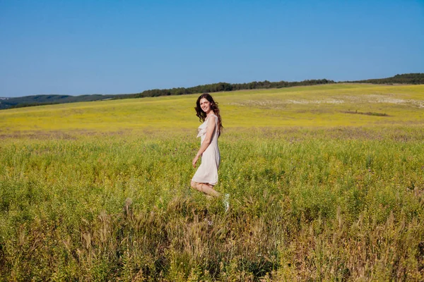 A beautiful woman in a dress walking in a field in nature — Stock Photo, Image