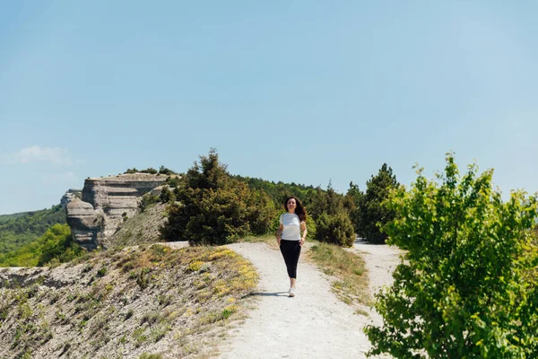 Brunette woman walking along a mountain road looks at the nature of the journey — Stock Photo, Image