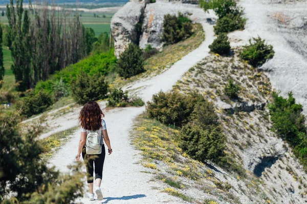 Brunette woman walking along a mountain road looks at the nature of the journey — Stock Photo, Image