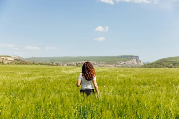 Beautiful brunette woman walking through a field of wheat looks at the nature — Stock Photo, Image