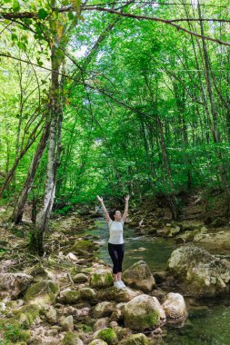 Güzel bir kadın yeşil orman doğa yolculuğunda bir dağ nehrinin kıyısında yürüyor.