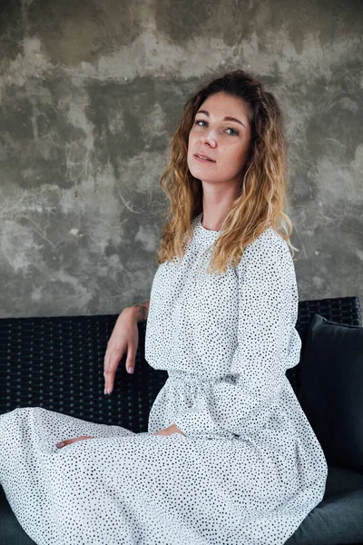 Portrait of a beautiful fashionable woman in a light dress on the loft sofa — Stock Photo, Image