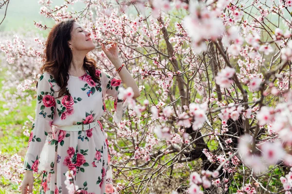 Baharda çiçek açan ağaçların bahçesinde elbiseli güzel bir kadın. — Stok fotoğraf