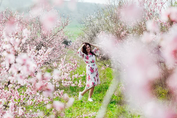 Baharda çiçek açan ağaçların bahçesinde elbiseli güzel bir kadın. — Stok fotoğraf