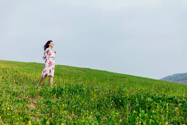Een mooie vrouw in een jurk in een groen veld kijkt naar het landschap — Stockfoto