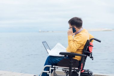 Tekerlekli sandalyede engelli bir adam akıllı telefondan konuşuyor.