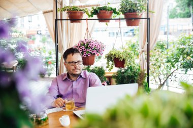 Bir adam bilgisayarda çalışıyor ve bir restoranda yemek yiyor.
