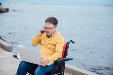 Tekerlekli sandalyede engelli bir adam akıllı telefondan konuşuyor.