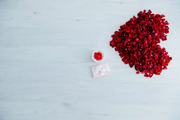 Pétalos de rosa roja y regalos sobre un fondo claro — Foto de Stock