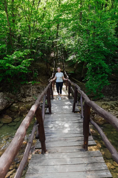 Yeşil bir orman gezisinde köprüden geçen bir kadın. — Stok fotoğraf