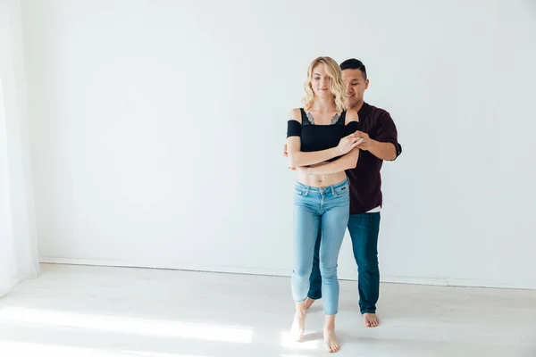 Um homem e uma mulher dançam bachata à música em uma sala branca — Fotografia de Stock