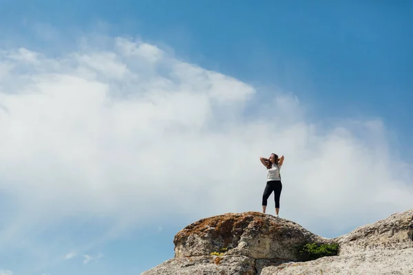 A beautiful woman looks at the view on top of a cliff on a cliff on a journey — Stock Photo, Image