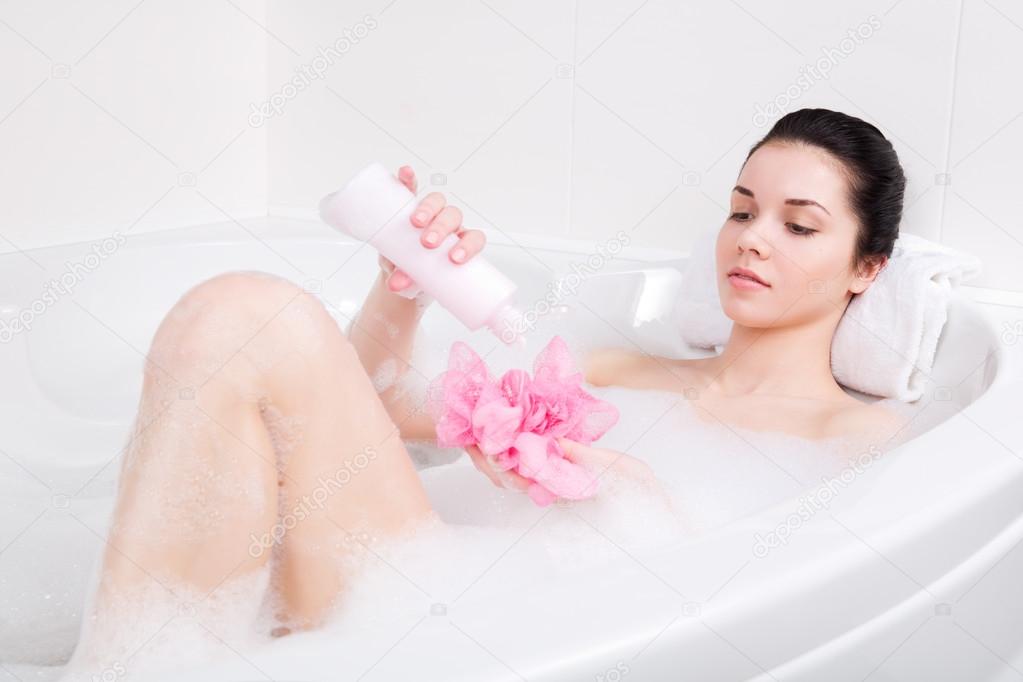 young woman in a bath with foam sponge in hand