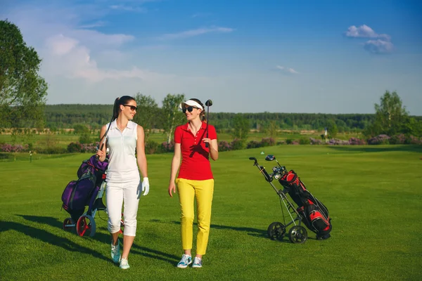 Duas mulheres bonitas golfistas andando no campo de golfe — Fotografia de Stock