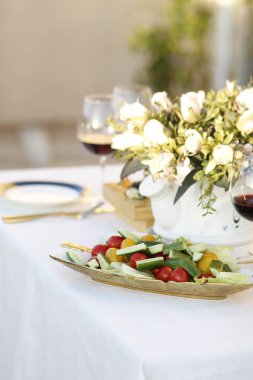 Bir tabak şarap, bir şişe şarap ve vazoda beyaz bir çiçek.