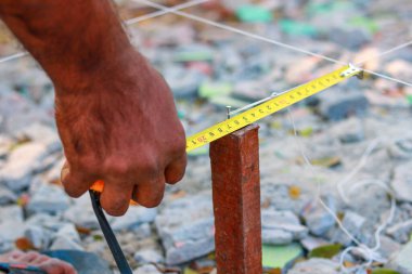 Bant ölçüsüyle ev düzeni için arazi ölçümleri yapan bir inşaat işçisinin yakın çekimi.