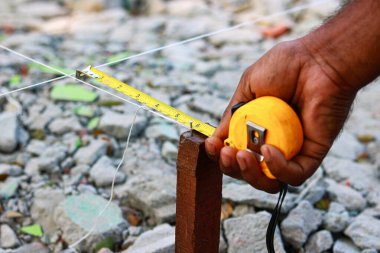 Bant ölçüsüyle ev düzeni için arazi ölçümleri yapan bir inşaat işçisinin yakın çekimi.
