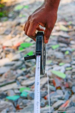 Bant ölçüsüyle ev düzeni için arazi ölçümleri yapan bir inşaat işçisinin yakın çekimi.