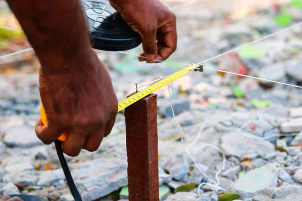 Bant ölçüsüyle ev düzeni için arazi ölçümleri yapan bir inşaat işçisinin yakın çekimi.