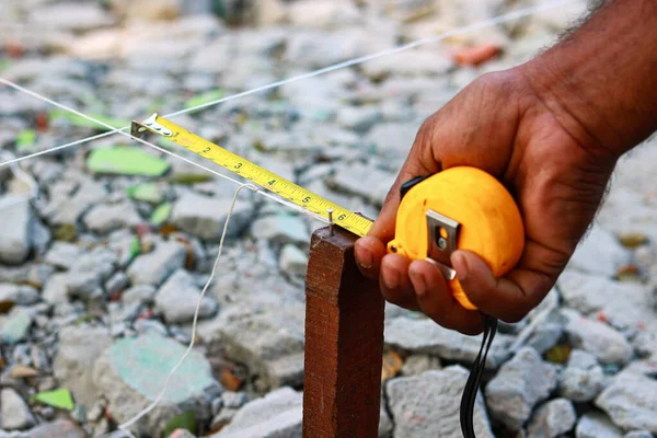 Bant ölçüsüyle ev düzeni için arazi ölçümleri yapan bir inşaat işçisinin yakın çekimi.