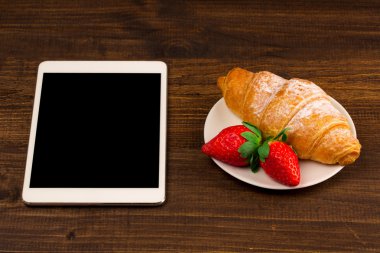 Kahvaltı ile taze kruvasanlar, rustik ahşap arka plan, üstten görünüm üzerinde taze çilek. tablet PC.