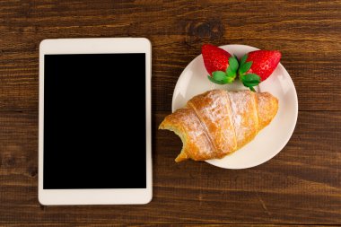 Kahvaltı ile taze kruvasanlar, rustik ahşap arka plan, üstten görünüm üzerinde taze çilek. tablet PC.