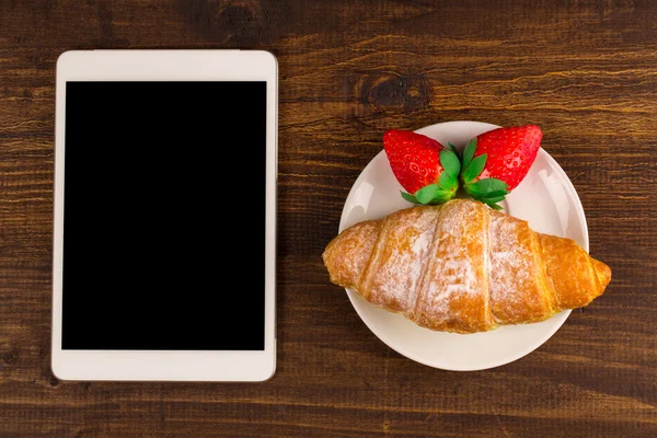 Kahvaltı ile taze kruvasanlar, rustik ahşap arka plan, üstten görünüm üzerinde taze çilek. tablet PC.