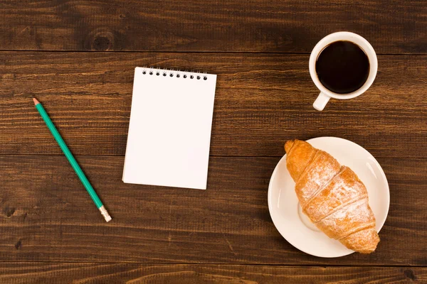 Frukost med kopp svart kaffe, croissanter, anteckningsbok med en penna — Stockfoto