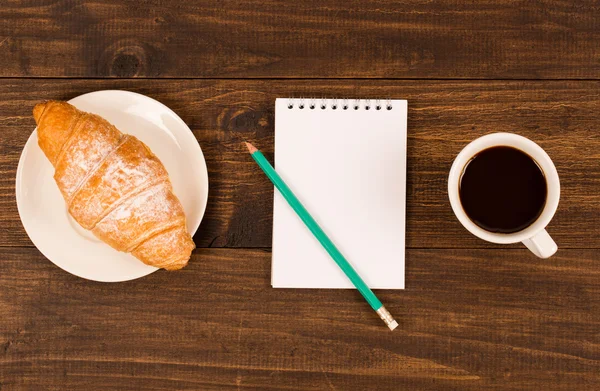 Frukost med kopp svart kaffe, croissanter, anteckningsbok med en penna — Stockfoto