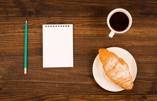 Frukost med kopp svart kaffe, croissanter, anteckningsbok med en penna — Stockfoto