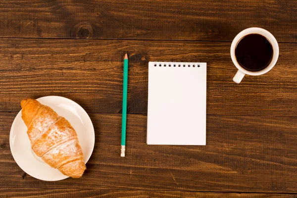 Frukost med kopp svart kaffe, croissanter, anteckningsbok med en penna — Stockfoto
