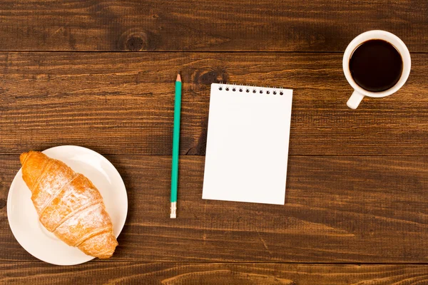 Frukost med kopp svart kaffe, croissanter, anteckningsbok med en penna — Stockfoto