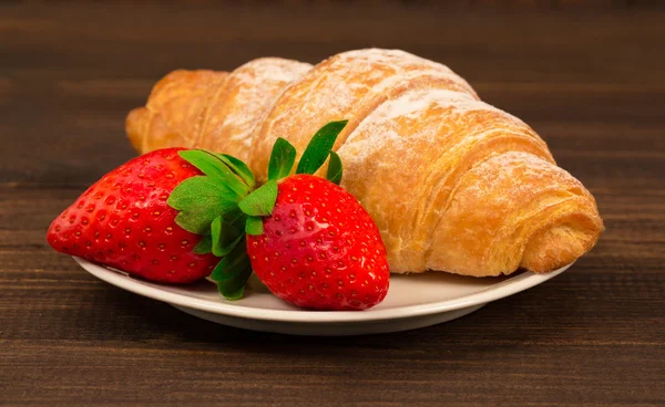 Färska franska croissant och jordgubb på brun träbord bakgrund — Stockfoto