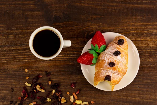 Una taza de té negro con frutas secas, croissant con fresa y fondo de mesa de madera. Arriba wiev . — Foto de Stock