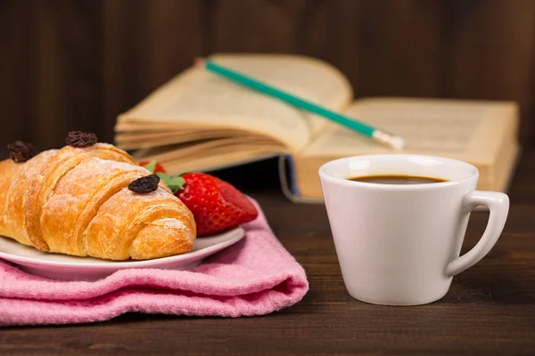 Kopp kaffe och en croissant och bok — Stockfoto