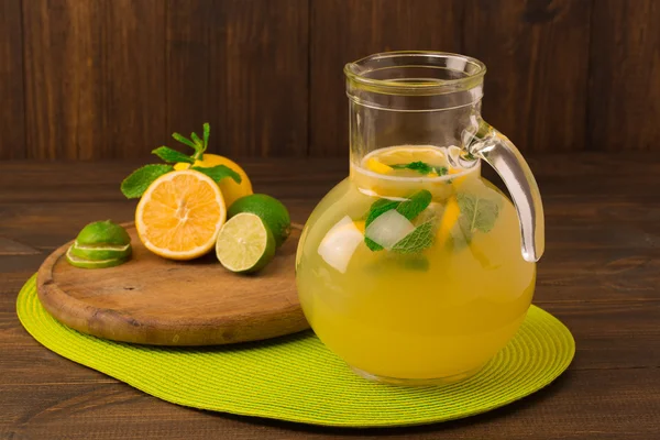 Lemonade with fresh lemon and mint in glass jug on wooden background — Stock Photo, Image